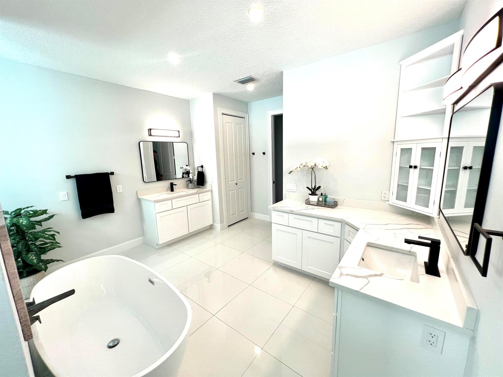 A modern bathroom features white cabinetry, marble-look countertops, a freestanding tub, and black hardware — 6660 49th, Vero Beach FL 32967, VERO BEACH, FL
