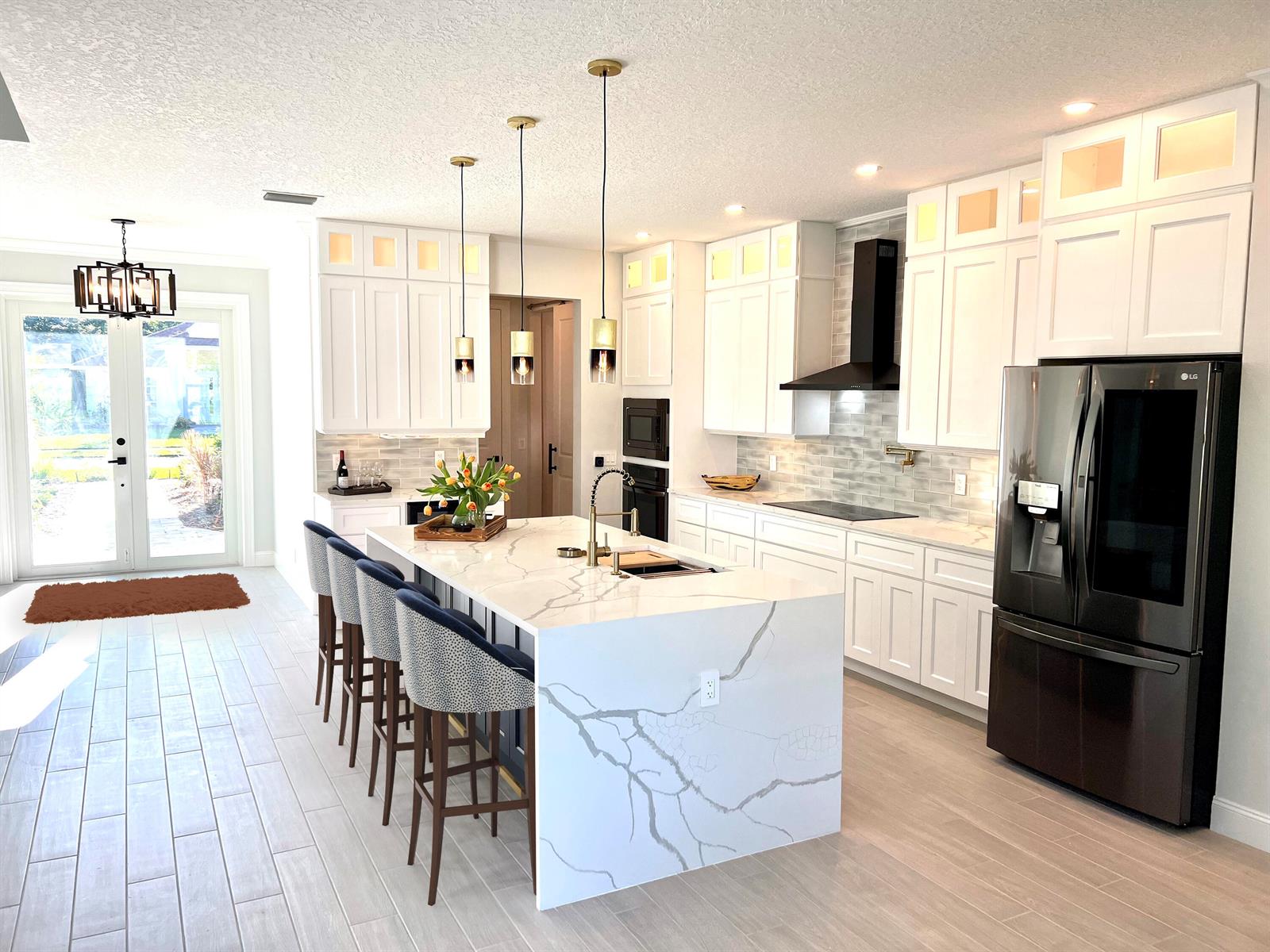 A modern kitchen features white cabinetry, a marble-topped island with bar stools, and stainless appliances — 6660 49th, Vero Beach FL 32967, VERO BEACH, FL