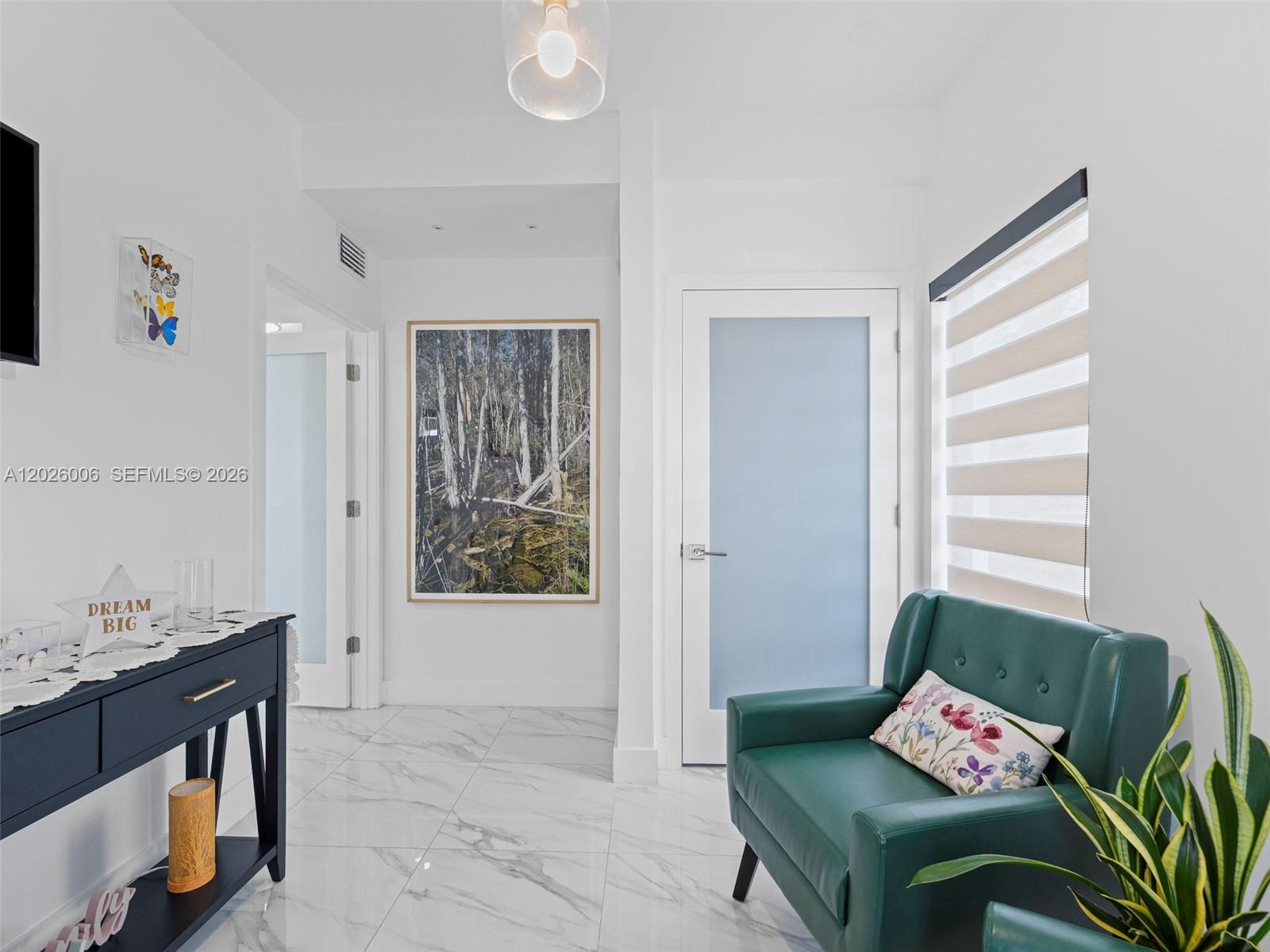 A bright entryway features white marble floors, a green armchair, and a framed forest print — 10700 SW 46th St, Miami FL 33165, MIAMI, FL