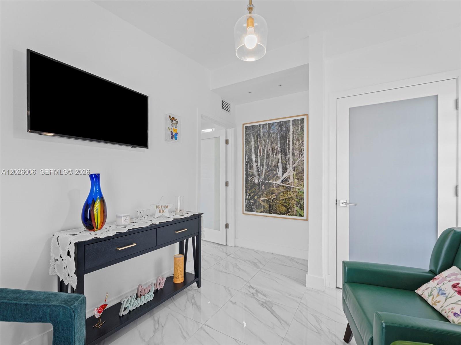 A bright hallway features white walls, marble-patterned tile floors, a console table, and a television — 10700 SW 46th St, Miami FL 33165, MIAMI, FL
