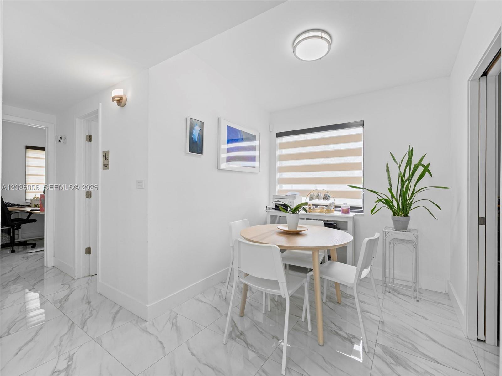 A dining area features a round wooden table, white chairs, and marble-patterned tile flooring — 10700 SW 46th St, Miami FL 33165, MIAMI, FL