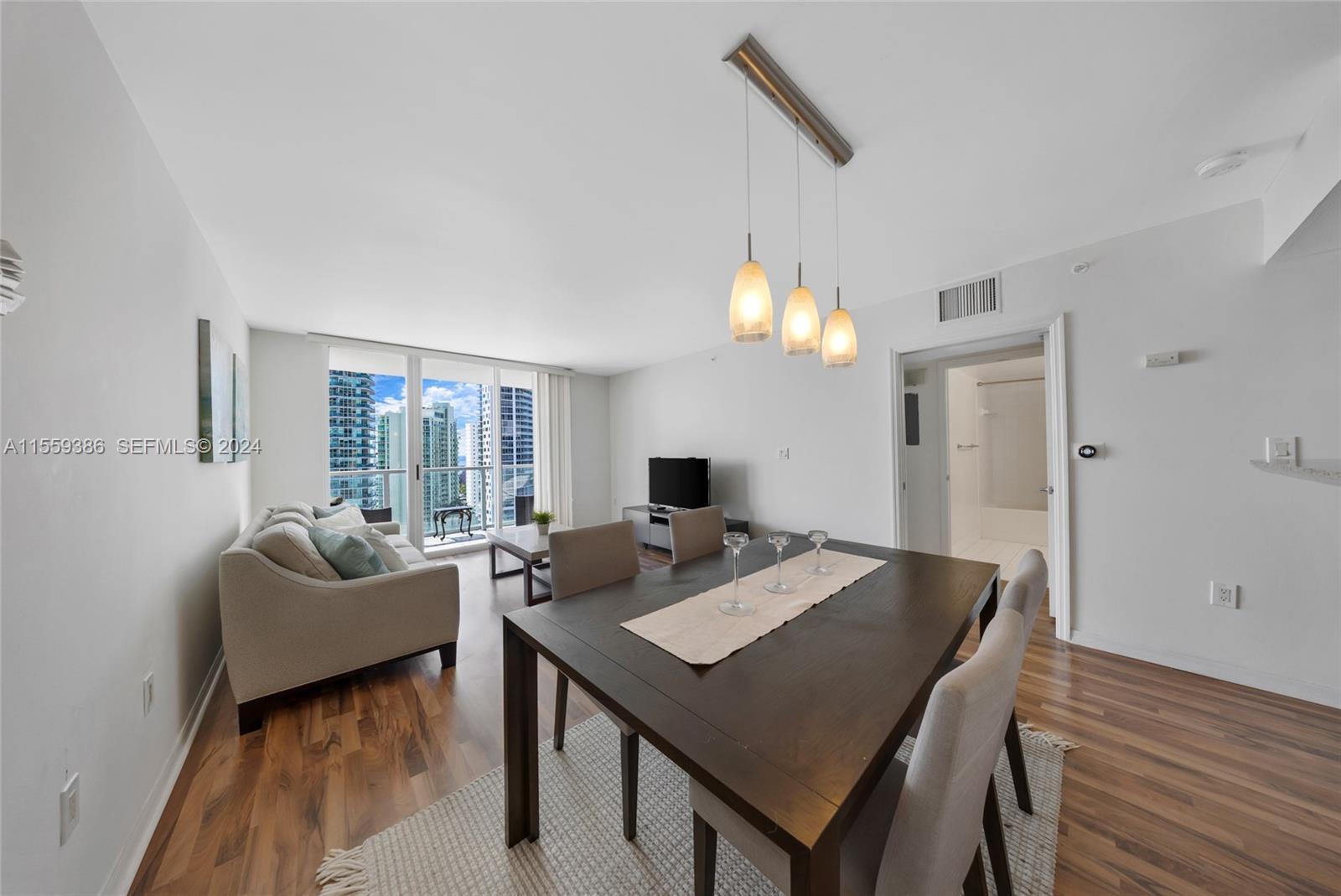 A dining area and living room with wood floors, modern lighting, and city balcony views — 1155 Brickell Bay Drive Apt 2207, Miami FL 33131, MIAMI, FL