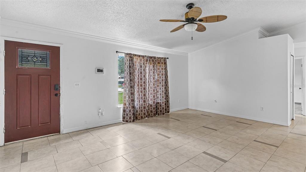 A living room with light tile flooring, white walls, a ceiling fan, and a front door — 1306 BORDEN COURT, VALRICO, FL