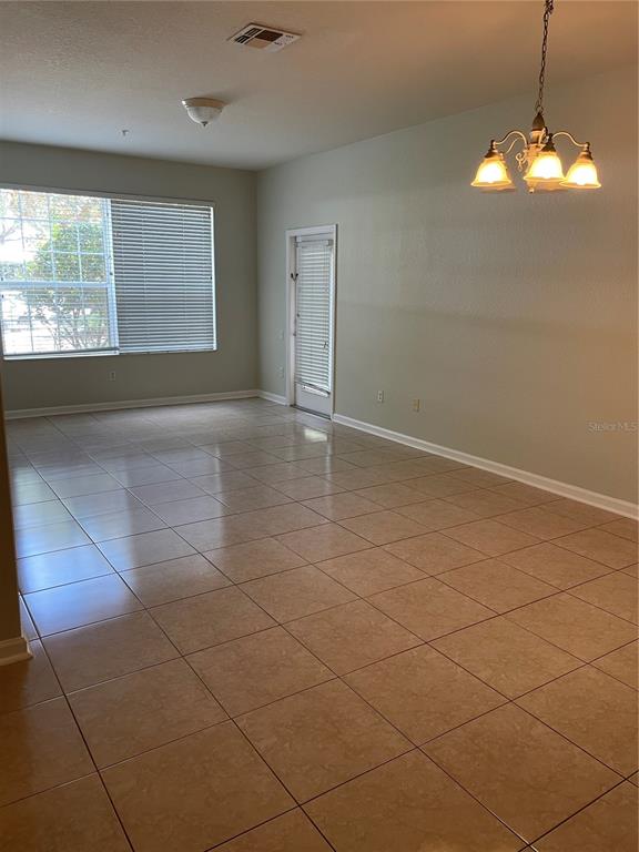 An empty room with beige tile flooring, a large window, and a chandelier — 3314 ROBERT TRENT JONES DRIVE UNIT 10901, ORLANDO, FL