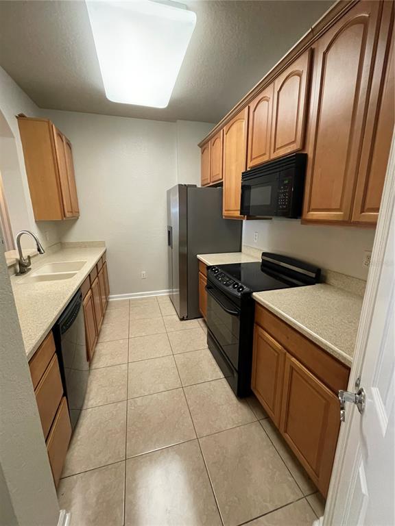 A galley kitchen features light wood cabinets, speckled countertops, and black appliances on tile flooring — 3314 ROBERT TRENT JONES DRIVE UNIT 10901, ORLANDO, FL