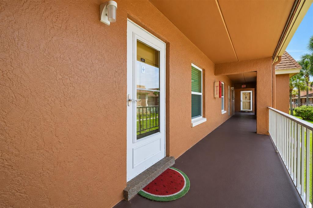 An exterior view of a building walkway with a white door and a watermelon mat — 12760 INDIAN ROCKS ROAD UNIT 570, LARGO, FL