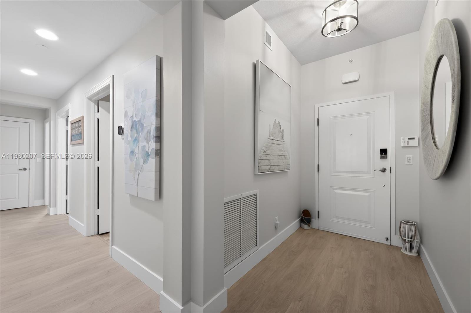 An entryway features light wood flooring, white walls, a round mirror, and two wall art pieces — 915 S Bay Colony Dr S, Juno Beach FL 33408, JUNO BEACH, FL