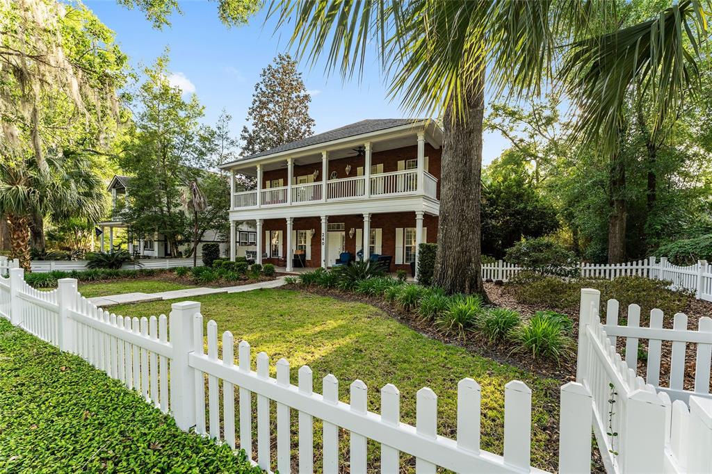 A two-story brick house with a double-decker porch sits behind a white picket fence — 240 SW 131ST STREET, NEWBERRY, FL