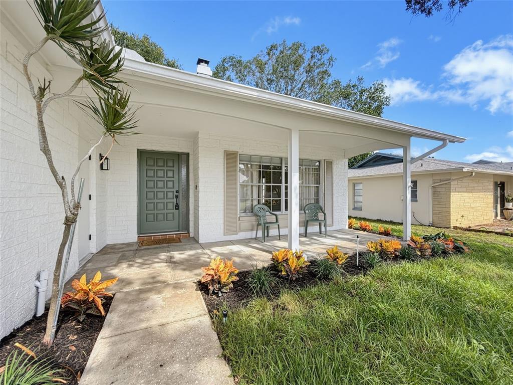A white brick house features a covered front porch, a green door, and landscaped garden beds — 10819 LOS SANTOS DR, PORT RICHEY, FL