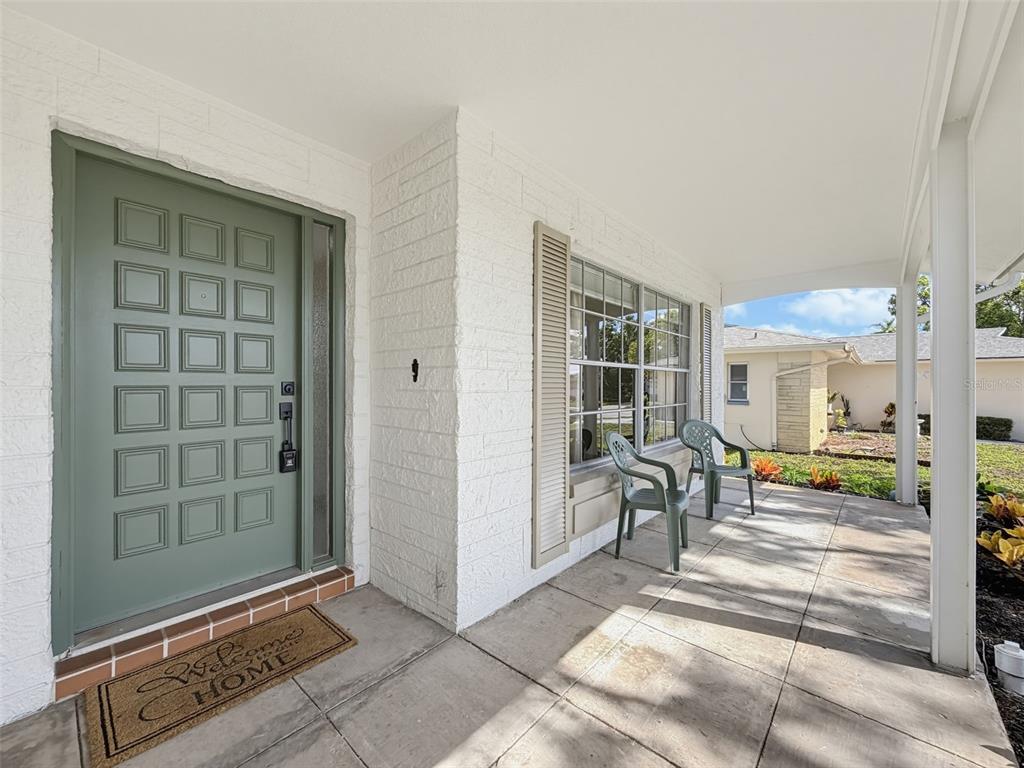A covered front porch features a sage green door, white brick walls, and two chairs — 10819 LOS SANTOS DR, PORT RICHEY, FL