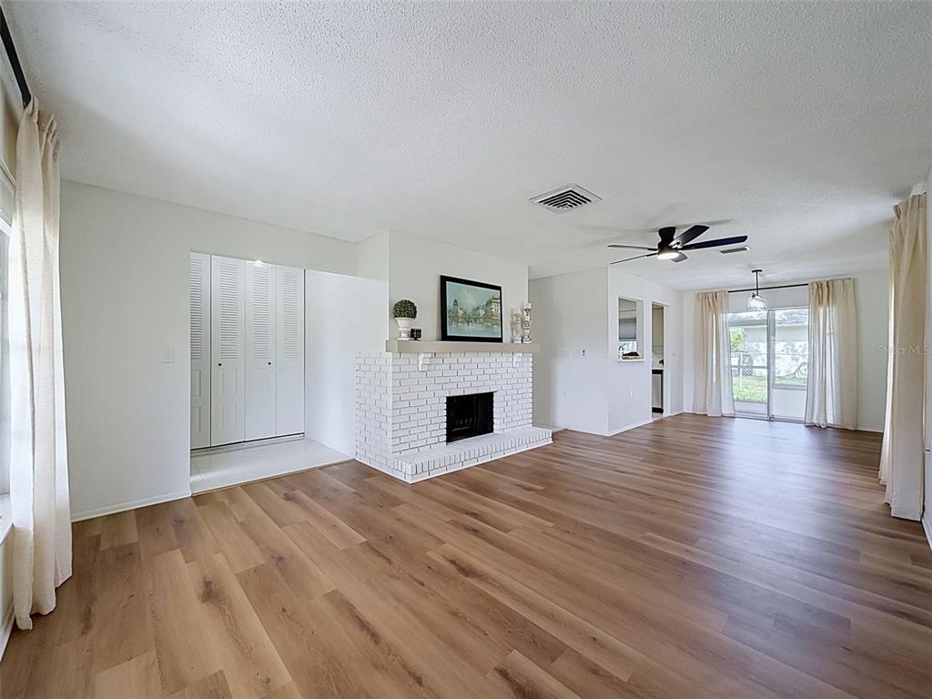 A living room with white walls, wood-look flooring, a white brick fireplace, and sliding glass doors — 10819 LOS SANTOS DR, PORT RICHEY, FL