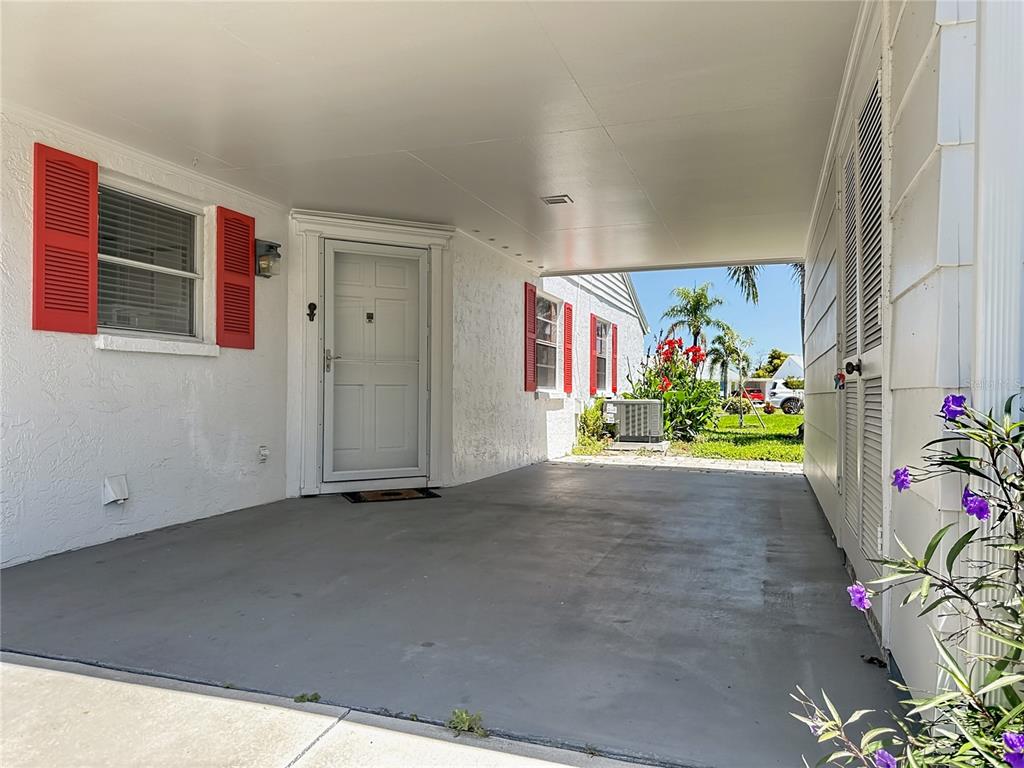 A covered carport with a white door, red shutters, and a concrete floor — 4523 W INDEPENDENCE DRIVE, BRADENTON, FL