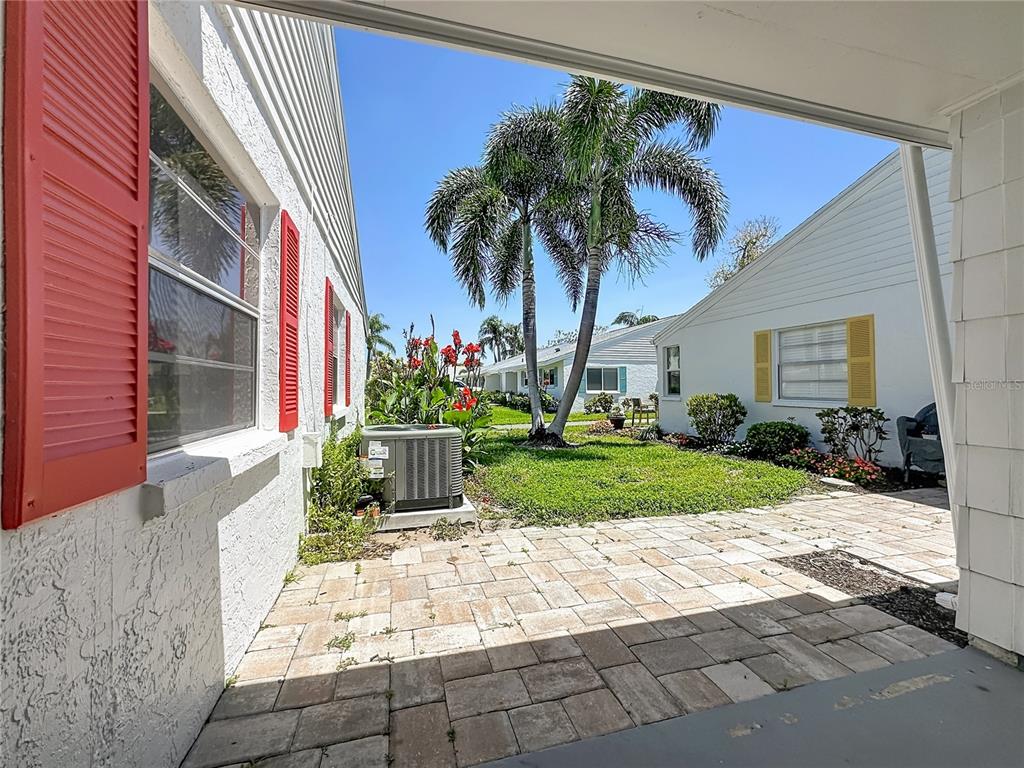 A paved patio sits between two white houses with red and yellow shutters and palm trees — 4523 W INDEPENDENCE DRIVE, BRADENTON, FL