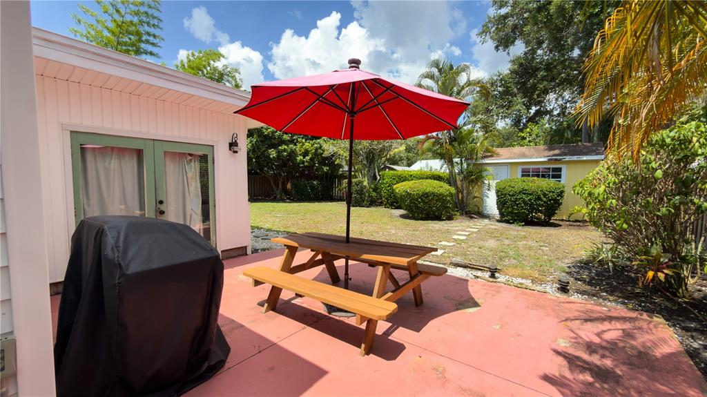 A red patio with a picnic table, umbrella, and grill sits outside a house — 2475 W PAULSTAN COURT, SARASOTA, FL