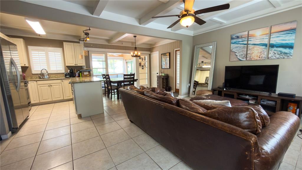 An open-concept living room and kitchen featuring tile floors, a leather sofa, and ceiling beams — 2475 W PAULSTAN COURT, SARASOTA, FL