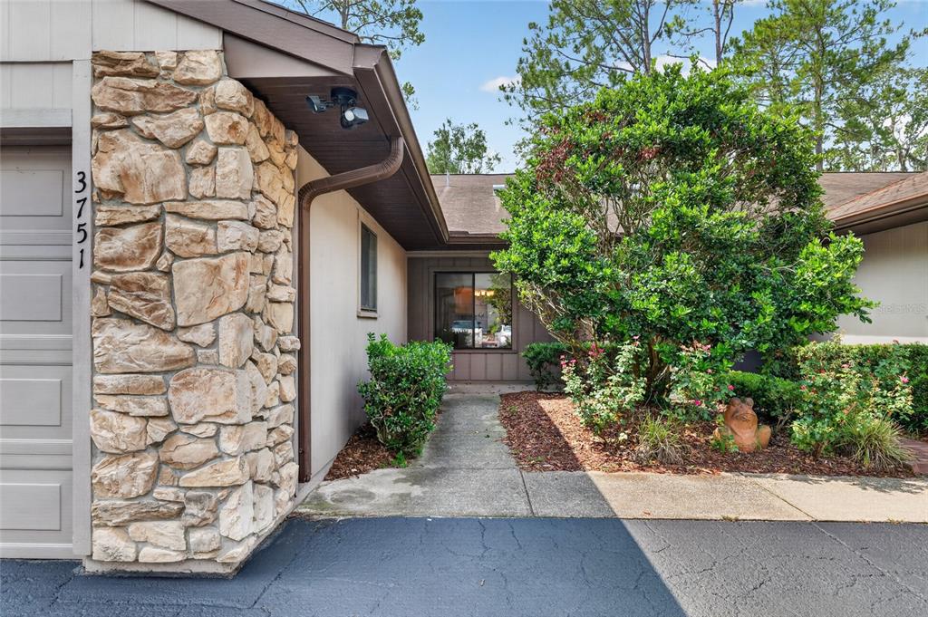 A stone-faced exterior wall with a house number and a walkway leading to the entrance — 3751 NW 53RD ROAD, GAINESVILLE, FL