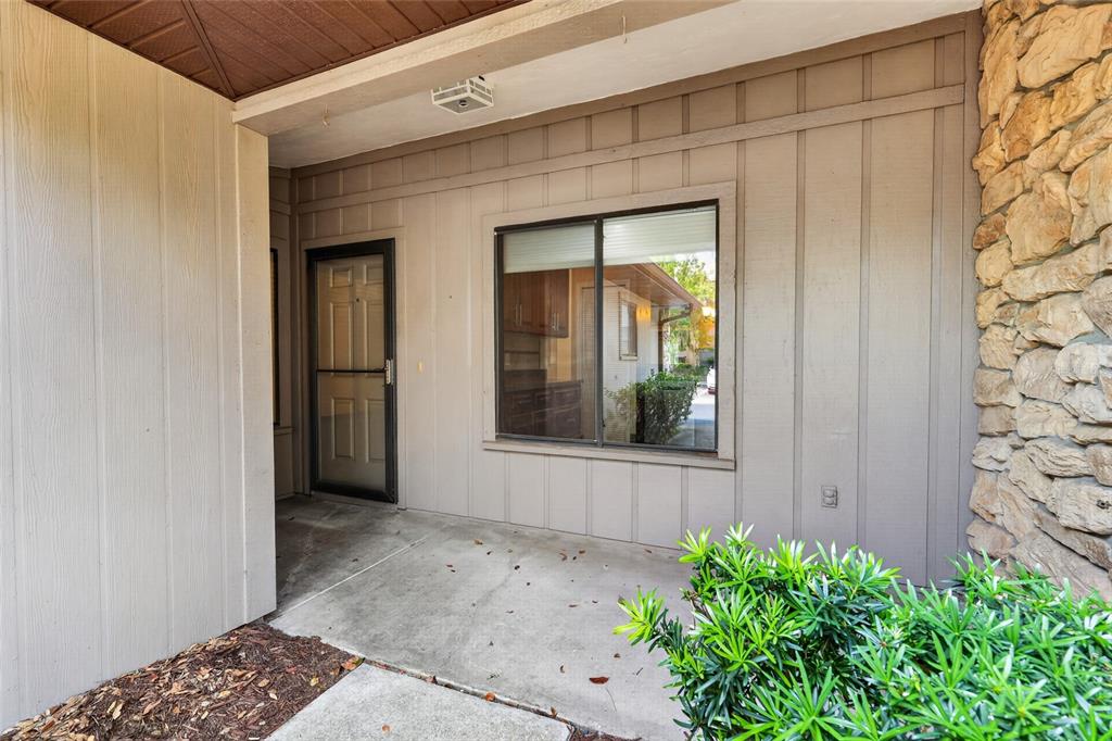 A covered concrete porch features a front door, a large window, and stone wall accents — 3751 NW 53RD ROAD, GAINESVILLE, FL