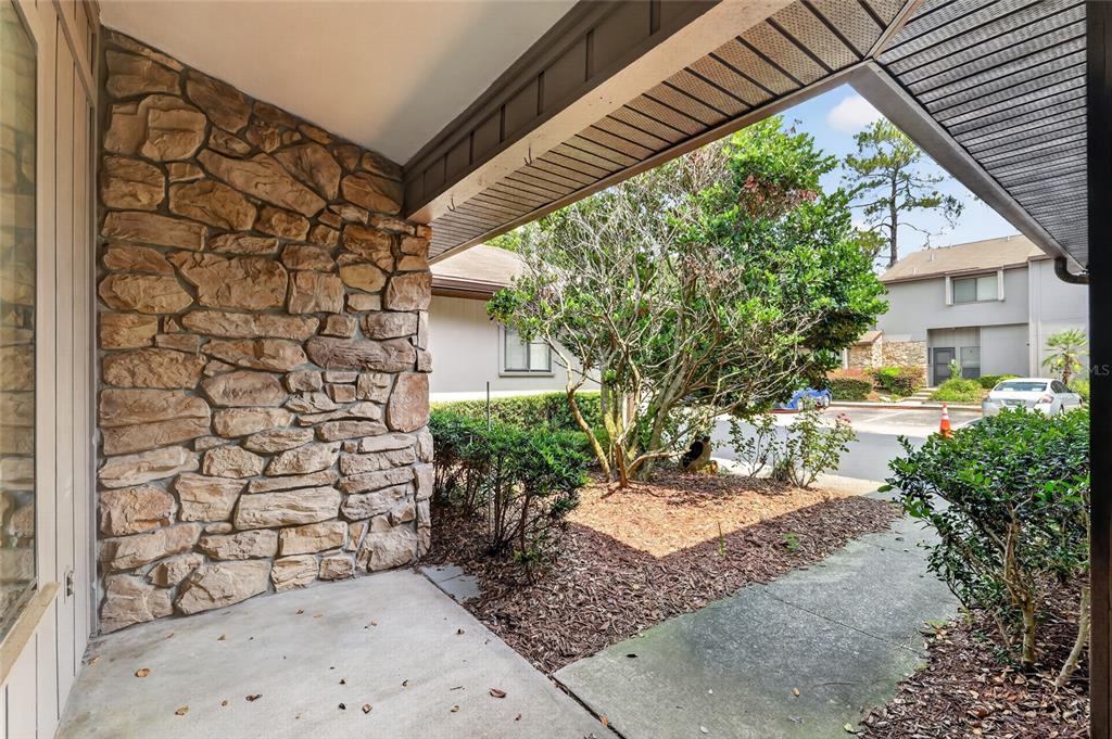 A covered concrete porch features a stone wall and overlooks a landscaped courtyard — 3751 NW 53RD ROAD, GAINESVILLE, FL