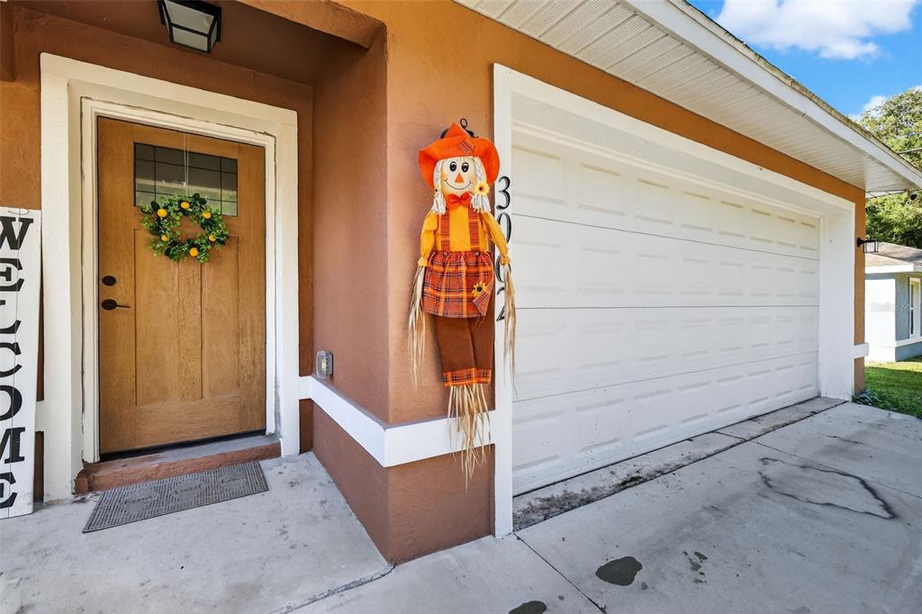 A tan house exterior features a wooden front door, a white garage door, and a scarecrow — 3062 SE 141ST PLACE, SUMMERFIELD, FL