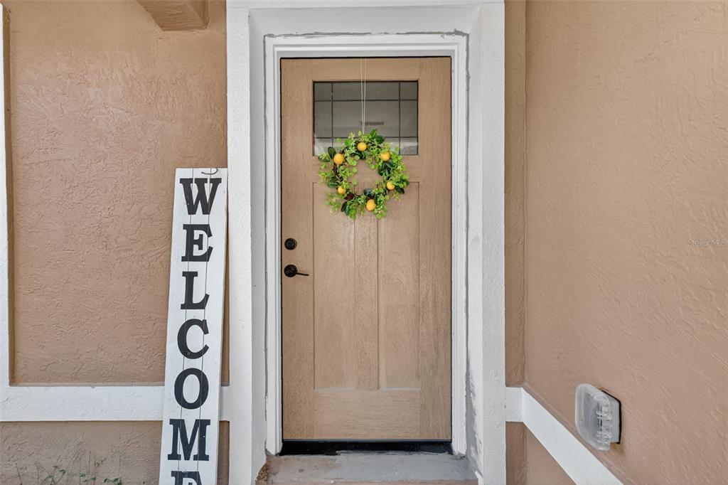 A tan front door with a lemon wreath stands next to a vertical welcome sign — 3062 SE 141ST PLACE, SUMMERFIELD, FL