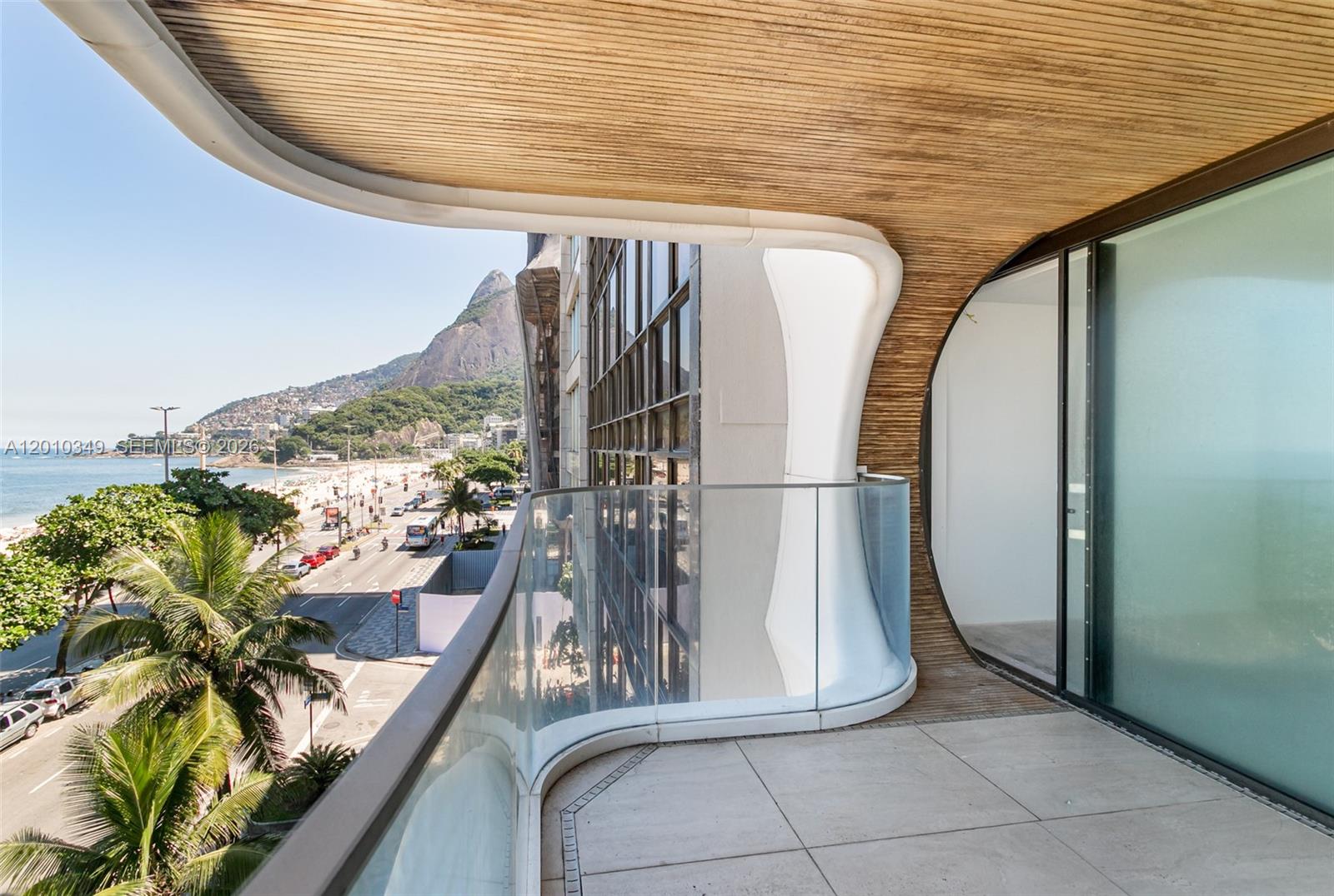 A modern balcony with a curved glass railing overlooks a coastal city and beach — FL