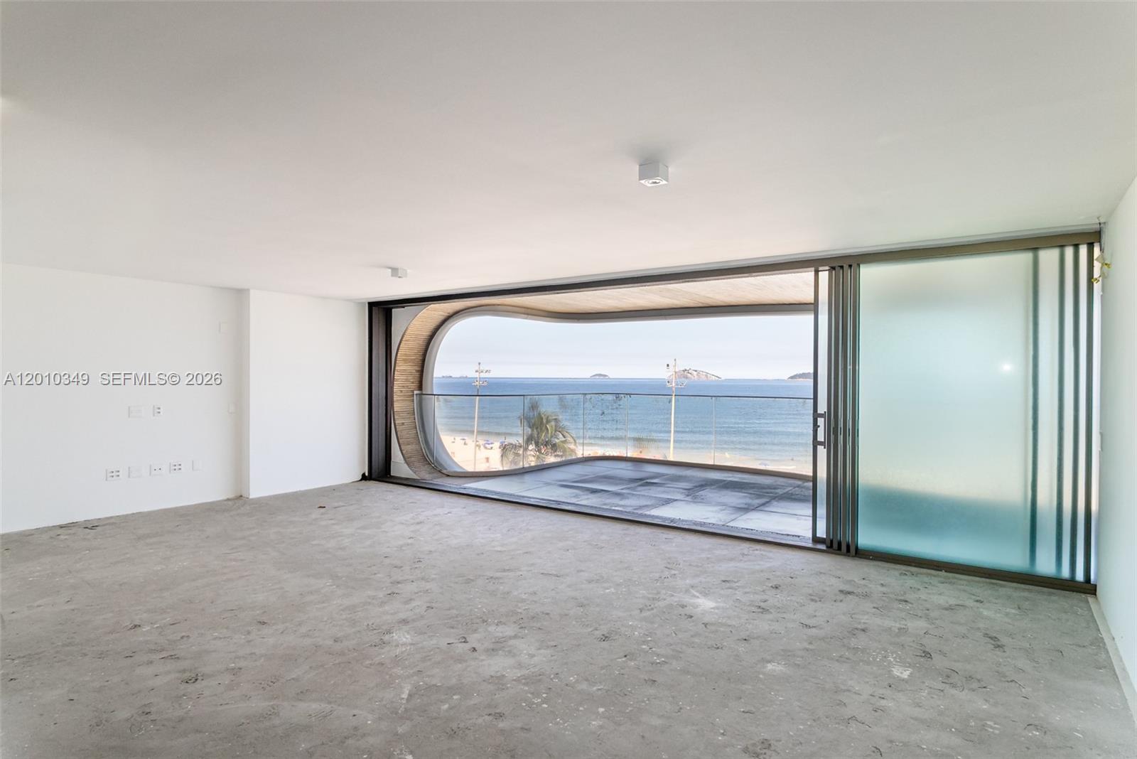 An unfinished room features a large, curved balcony opening with expansive ocean and beach views — FL