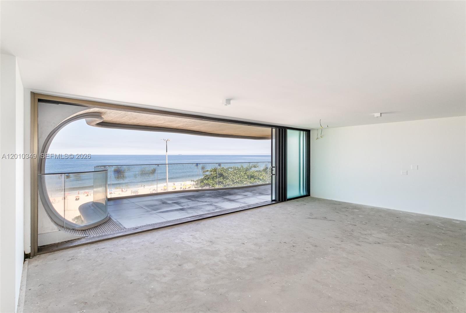 An unfinished room features a large sliding glass door opening to a curved oceanfront balcony — FL