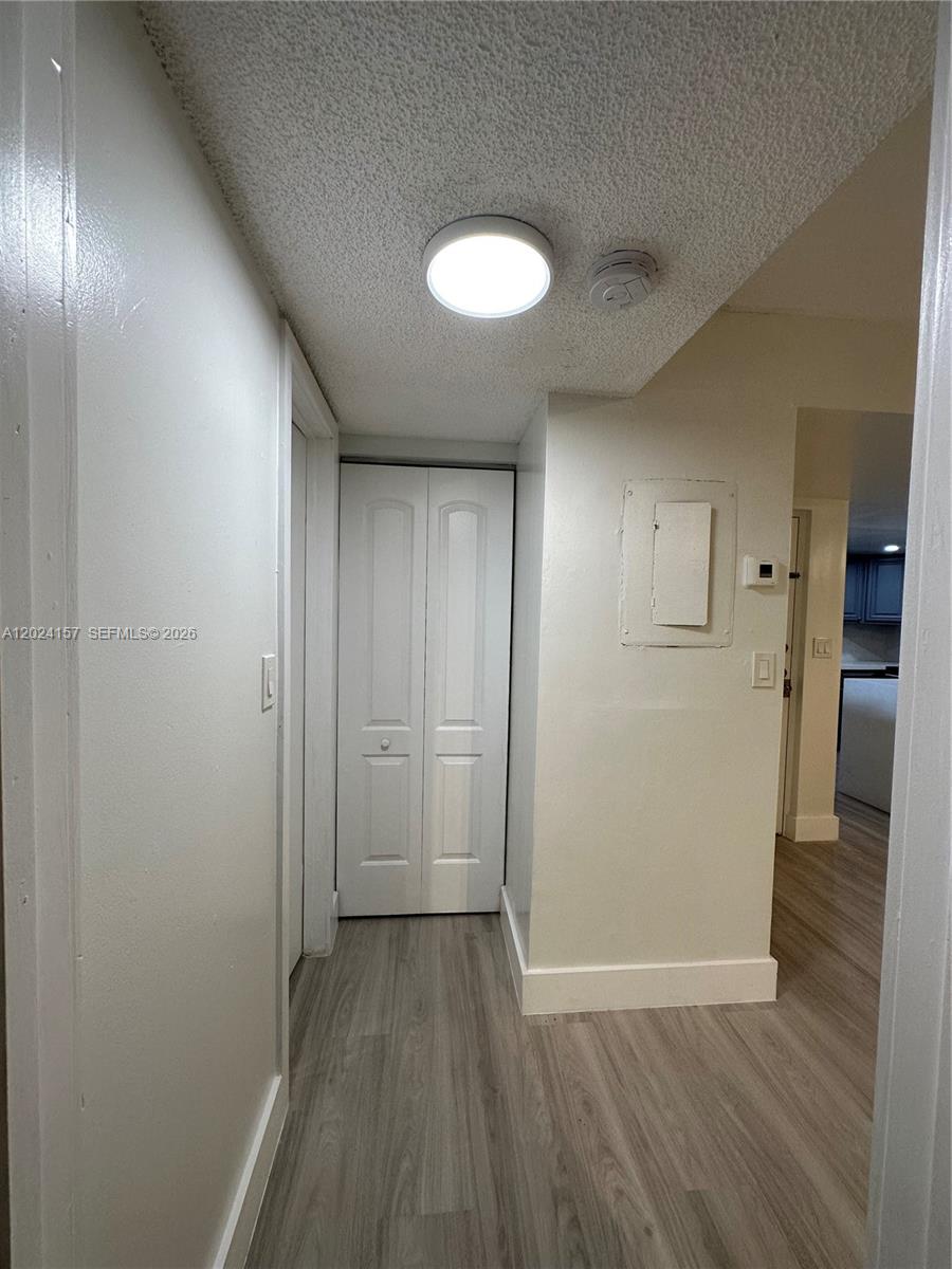 A hallway features light wood-look flooring, white walls, a popcorn ceiling, and a closet — 10813 NW 7th St # 11, Miami FL 33172, MIAMI, FL