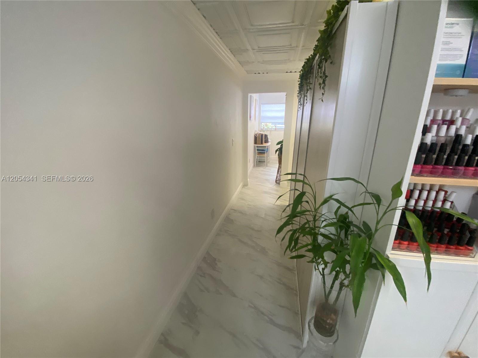 A hallway with marble-look tile flooring leads to a brightly lit room with a window — CORAL GABLES, FL
