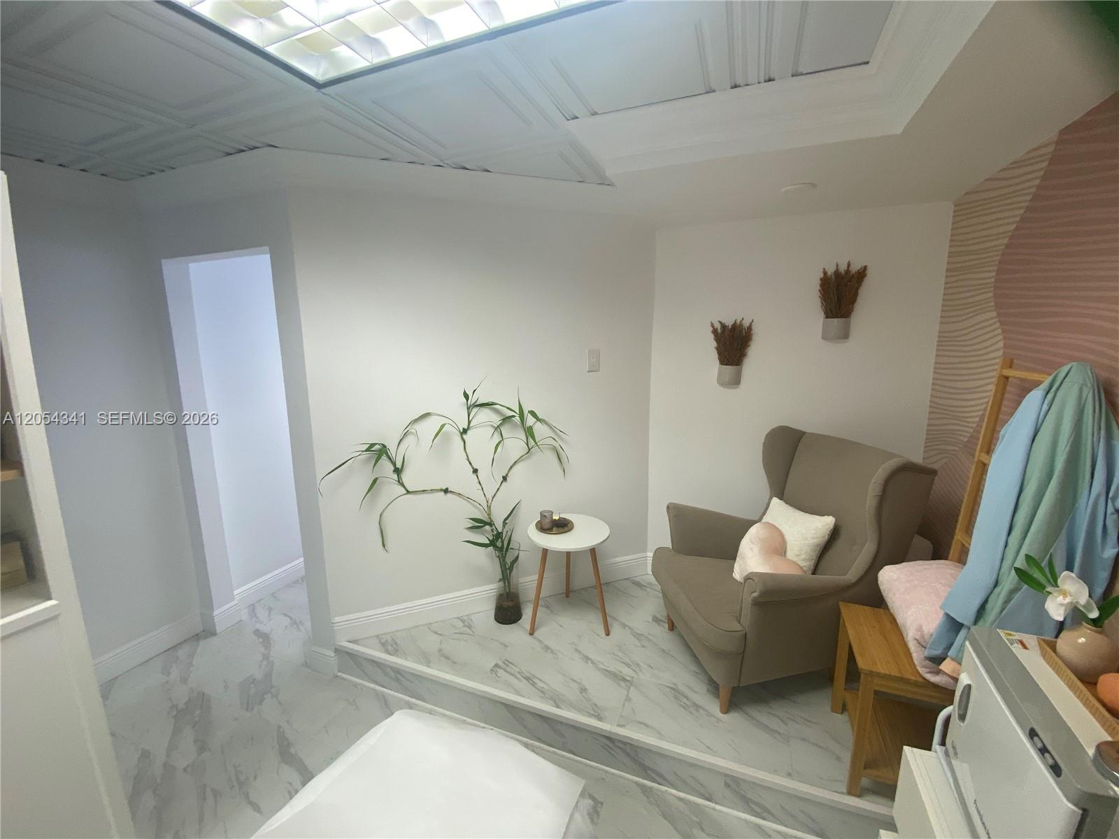 A small seating area features a beige armchair, a side table, and marble-look flooring — CORAL GABLES, FL