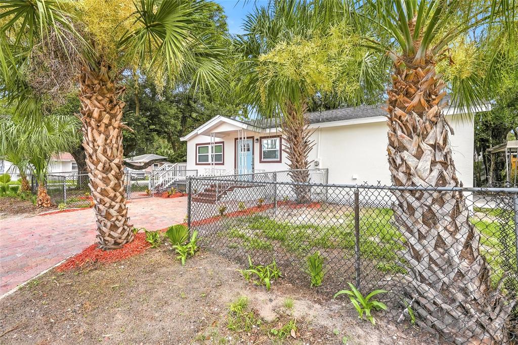 A white house with a light blue front door is viewed behind a chain-link fence — 1002 E SEWARD STREET, TAMPA, FL