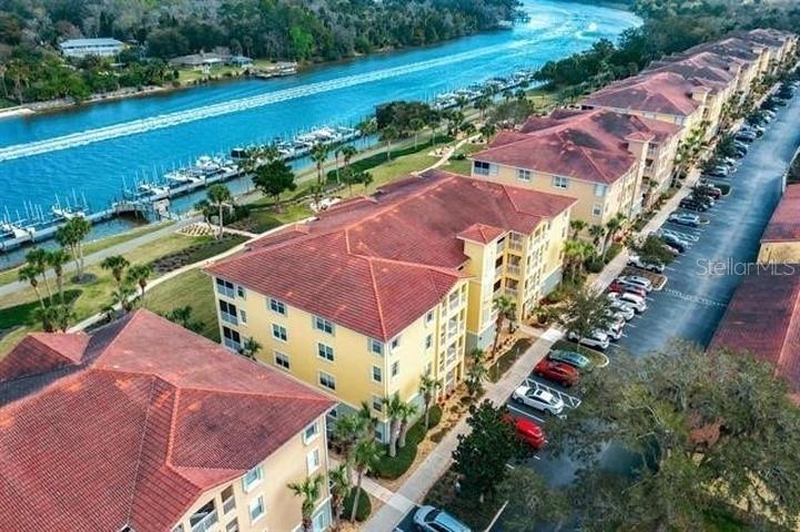 An aerial view shows multi-story apartment buildings with red roofs situated beside a canal — 700 CANOPY WALK LANE UNIT 734, PALM COAST, FL