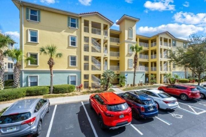 A multi-story yellow apartment building with a parking lot in the foreground — 700 CANOPY WALK LANE UNIT 734, PALM COAST, FL