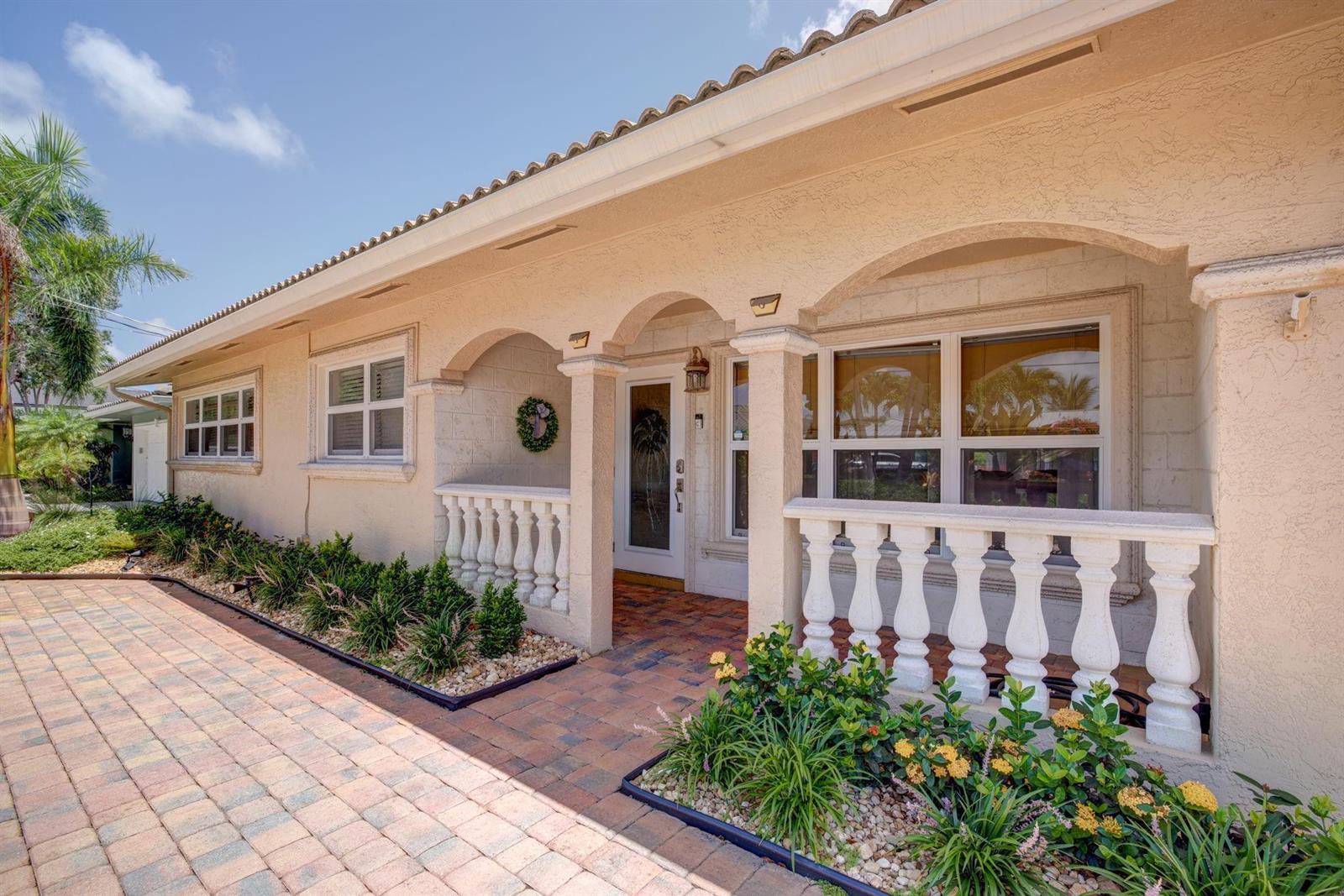 The exterior of a beige house features a paved walkway, arched entryway, and white balustrades — 1920 Waters Edge, Pompano Beach FL 33062, POMPANO BEACH, FL