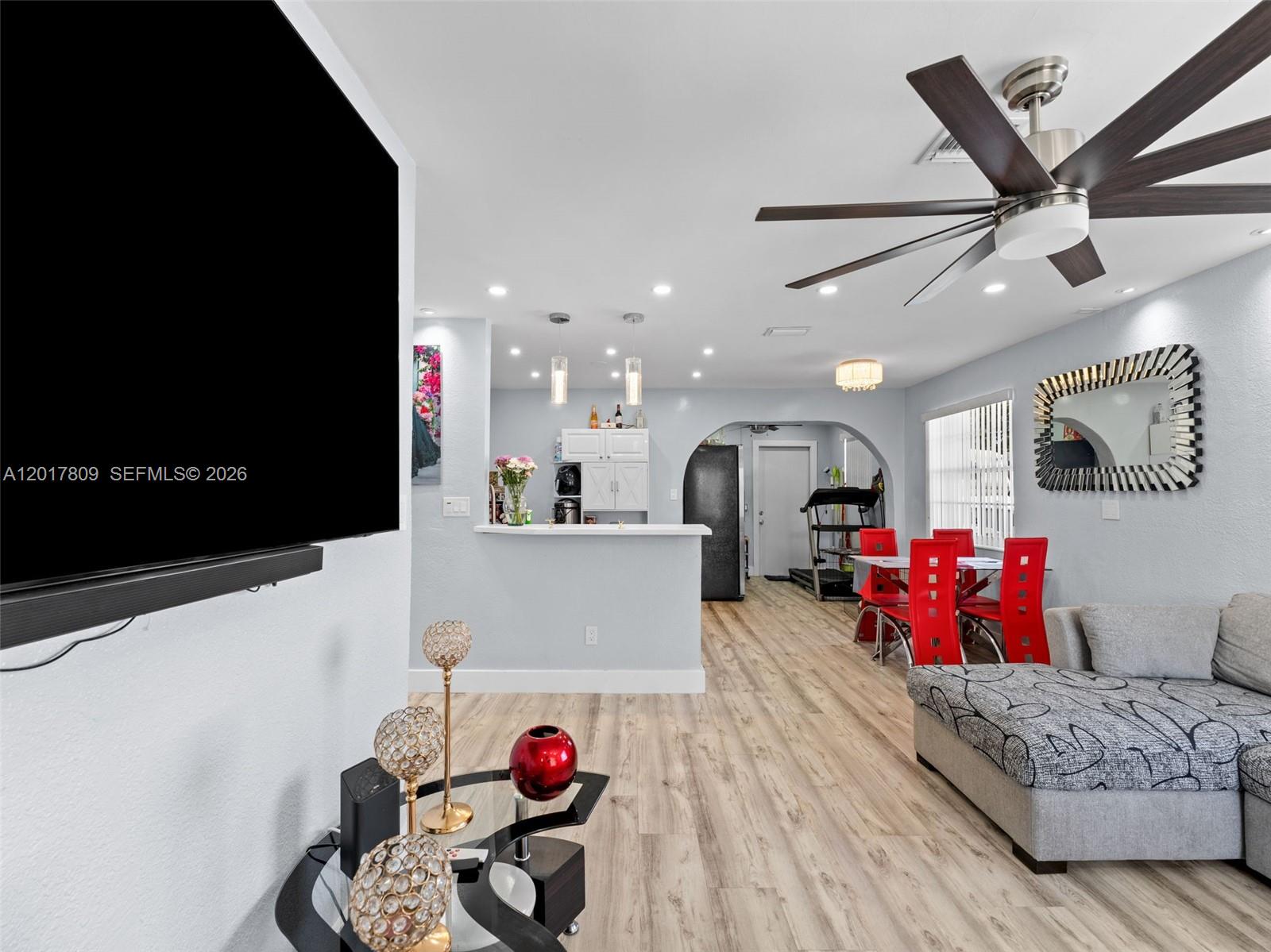 A living room with light wood floors, a grey sectional, and a dining area beyond — 6432 Perry St, Hollywood FL 33024, HOLLYWOOD, FL
