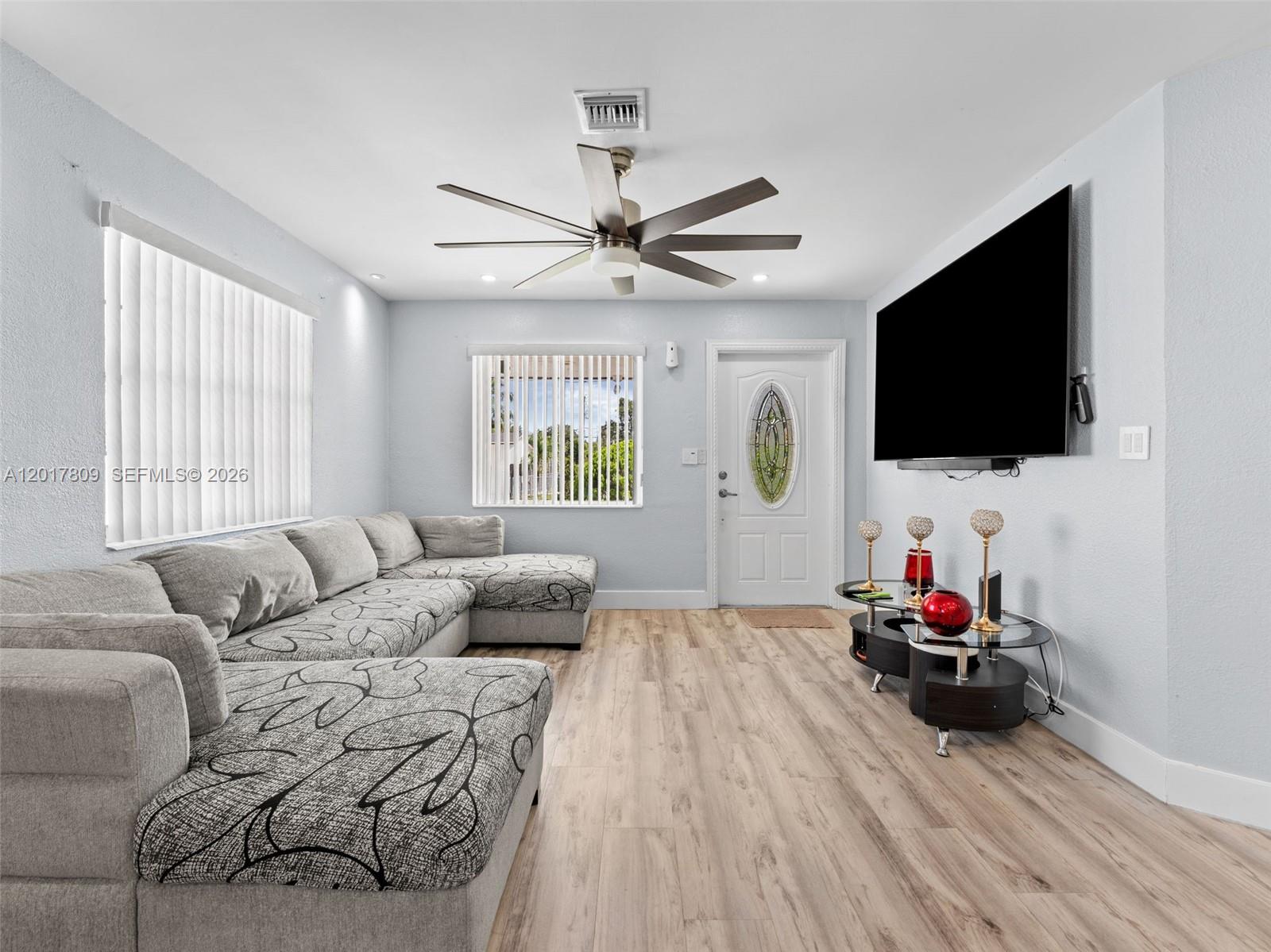 A living room features a gray sectional sofa, a wall-mounted television, and light wood flooring — 6432 Perry St, Hollywood FL 33024, HOLLYWOOD, FL