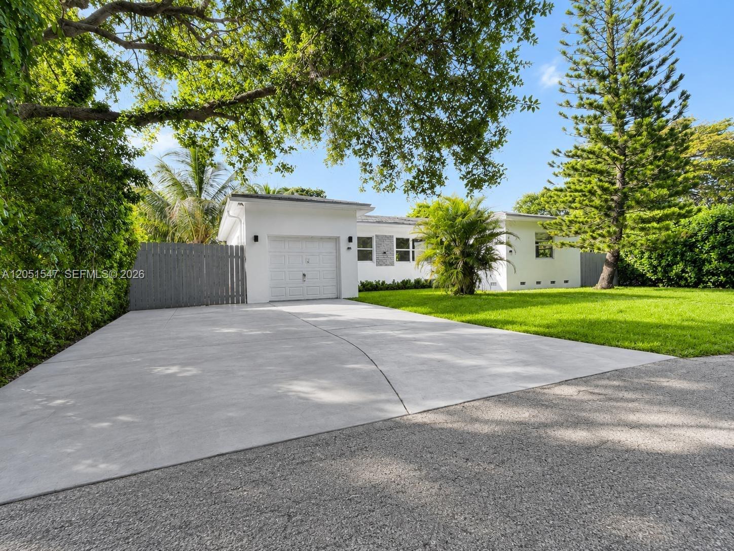 A white single-story house features a concrete driveway, a garage, and surrounding green landscaping — 859 NE 115th St, Biscayne Park FL 33161, BISCAYNE PARK, FL
