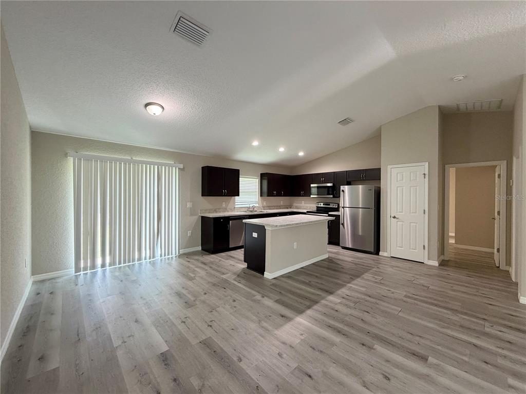 An open-concept kitchen and living area features dark cabinets, stainless steel appliances, and wood-look flooring — 1369 W DOLORES DRIVE, CITRUS SPRINGS, FL