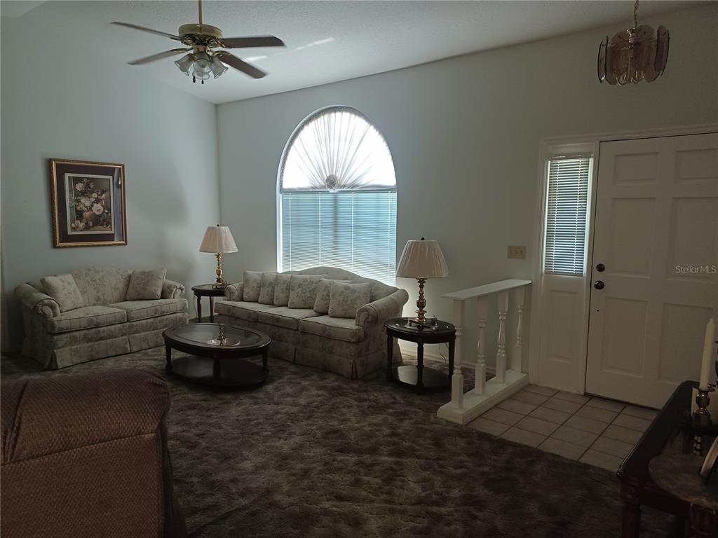 A living room features a vaulted ceiling, arched window, carpeted flooring, and two floral sofas — 805 VELMA COURT, TAVARES, FL