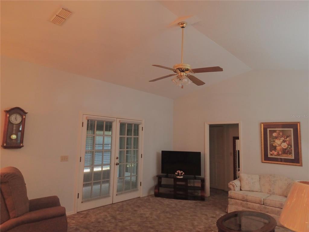 A living room features a vaulted ceiling, a ceiling fan, carpeted floors, and French doors — 805 VELMA COURT, TAVARES, FL