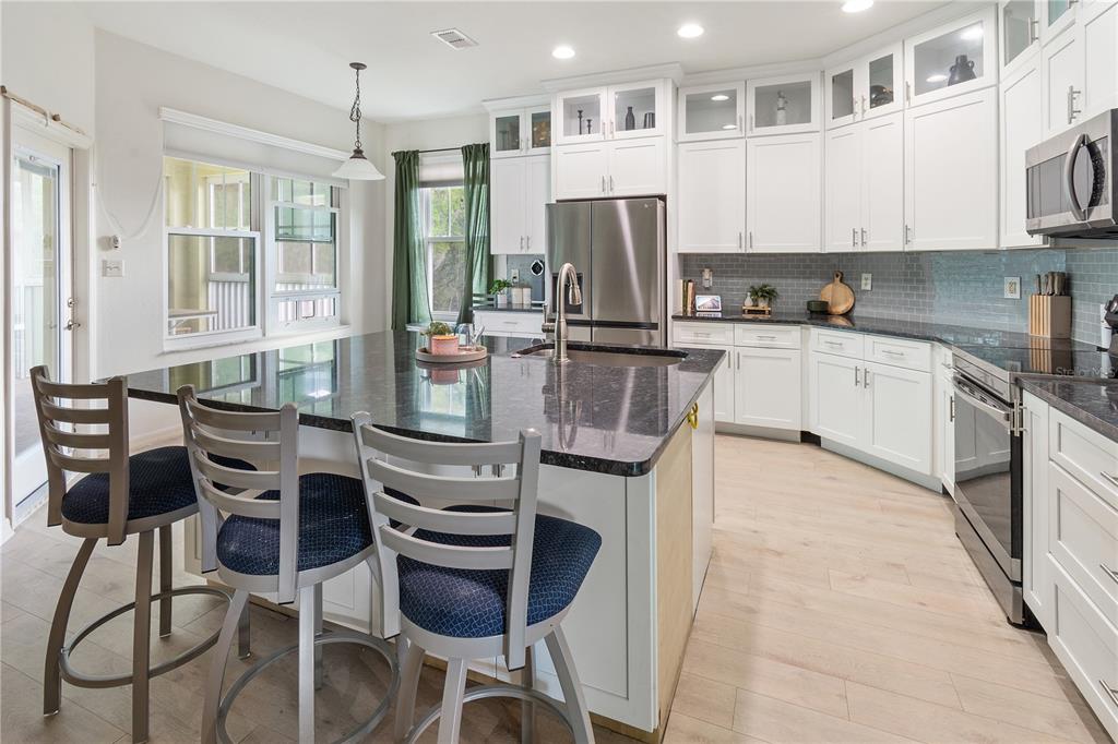 A kitchen features white cabinetry, a dark granite island with bar stools, and light flooring — 3818 SERENADE LANE UNIT 3818, LAKELAND, FL