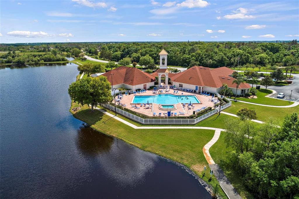 An aerial view shows a community swimming pool and clubhouse situated beside a large lake — 3818 SERENADE LANE UNIT 3818, LAKELAND, FL