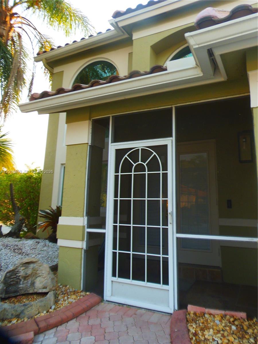 A screened-in front entryway features a white arched door and tan stucco exterior walls — 2608 NW 79th Ave, Margate FL 33063, MARGATE, FL