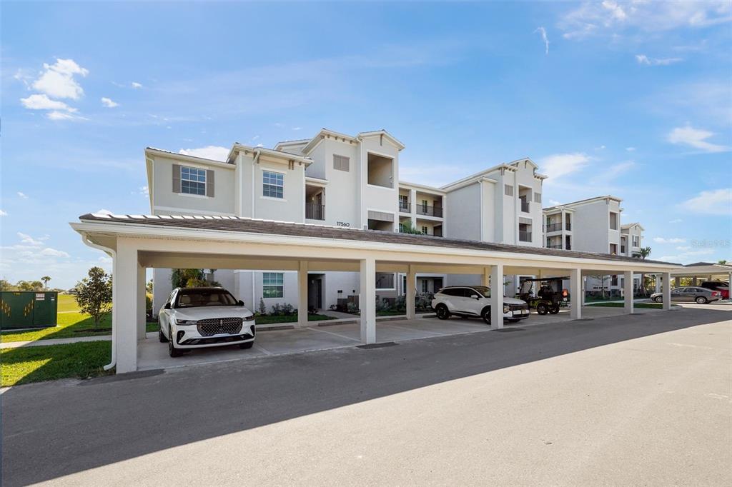 A multi-story apartment building features a covered parking structure with several parked vehicles — 17630 OPAL SAND DRIVE UNIT 102, VENICE, FL