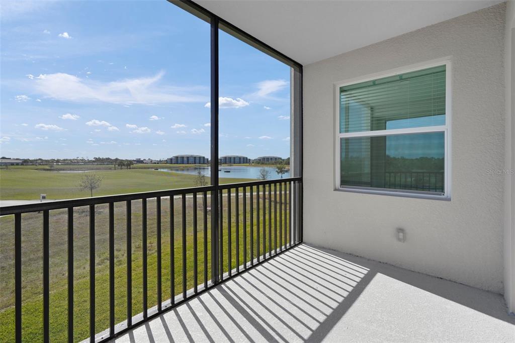 A screened-in balcony overlooks a grassy field and a pond under a blue sky — 17630 OPAL SAND DRIVE UNIT 102, VENICE, FL
