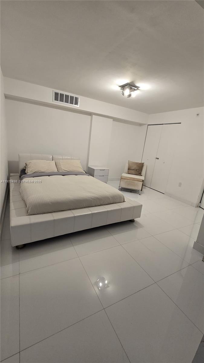 A bedroom features a low-profile white platform bed, white tile flooring, and a white closet — 9195 Collins Ave # 406, Surfside FL 33154, SURFSIDE, FL