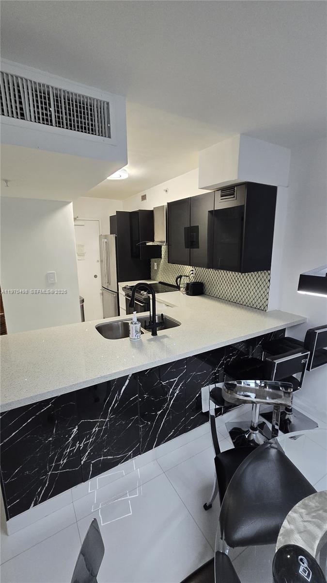 A kitchen features black cabinets, a marble-patterned island base, and white quartz countertops — 9195 Collins Ave # 406, Surfside FL 33154, SURFSIDE, FL