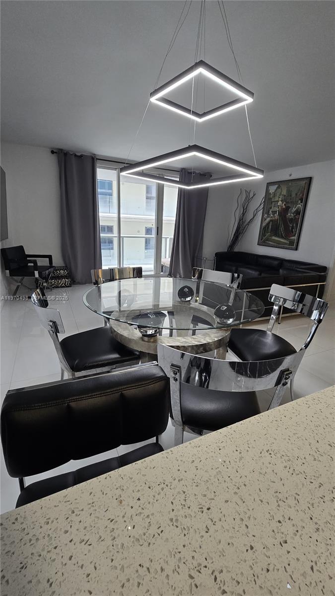 A dining area features a glass-topped table, modern square pendant lighting, and black chairs — 9195 Collins Ave # 406, Surfside FL 33154, SURFSIDE, FL