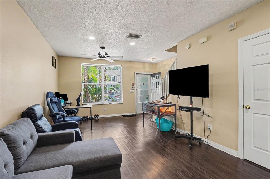 A living room features dark wood-look flooring, a gray sectional sofa, and a television stand — 6236 OSPREY LAKE CIRCLE, RIVERVIEW, FL