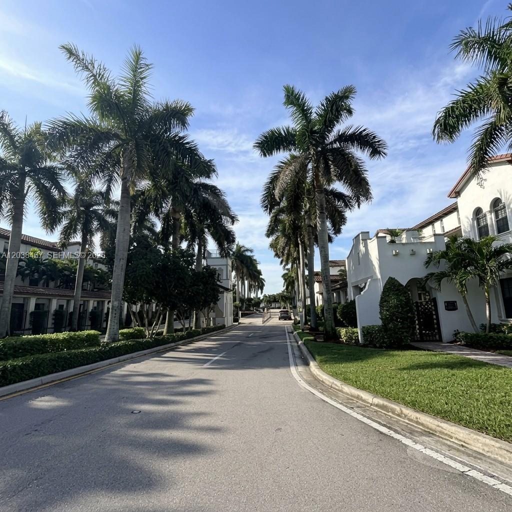 A paved road lined with palm trees leads toward white buildings under a blue sky — 11835 SW 27th St # 801, Miramar FL 33025, MIRAMAR, FL
